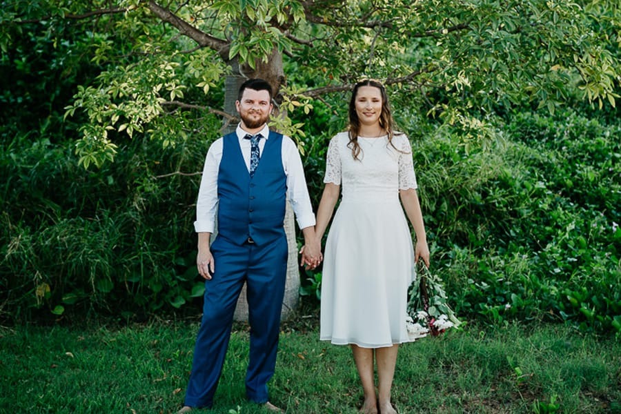 Couple in wedding attire holding hands under a tree