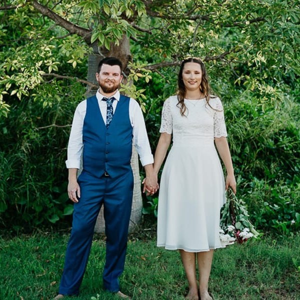 Couple in wedding attire holding hands under a tree