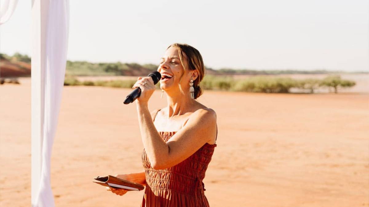 Woman in red dress singing with a microphone outdoors on a sunny day.
