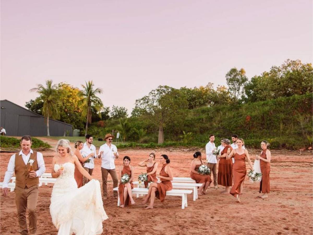 Wedding party walking on sandy beach, with a purple sky and lush greenery in the background.