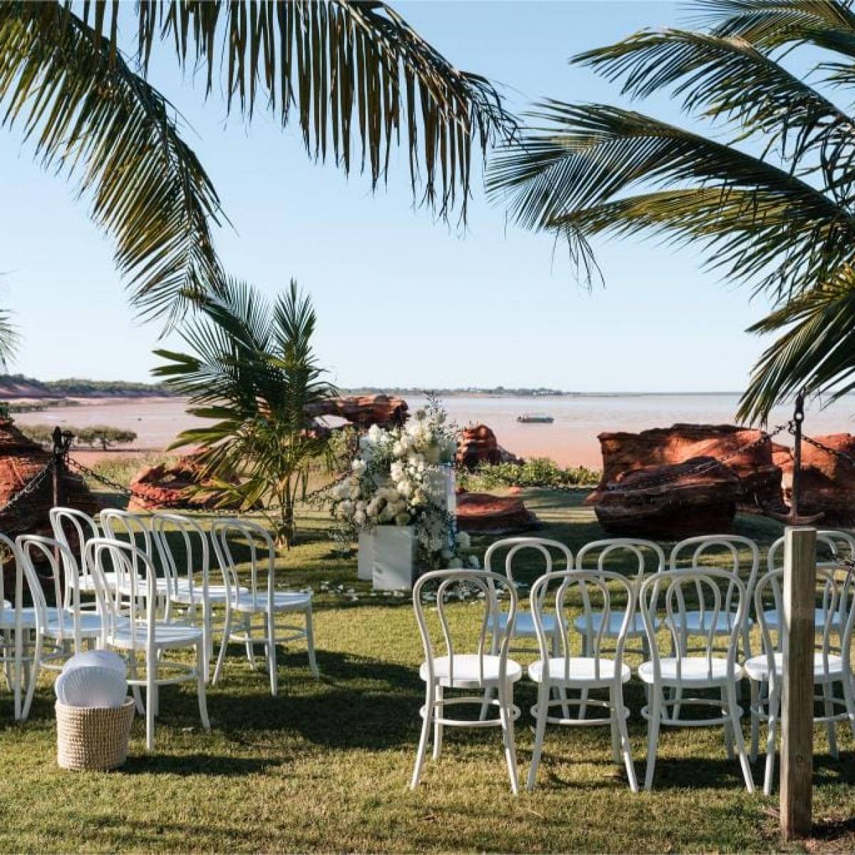 Outdoor wedding setup with white chairs, palm trees, and ocean view.