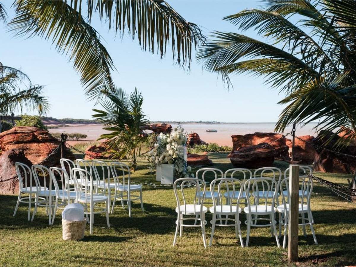 Outdoor wedding setup with white chairs, palm trees, and ocean view.