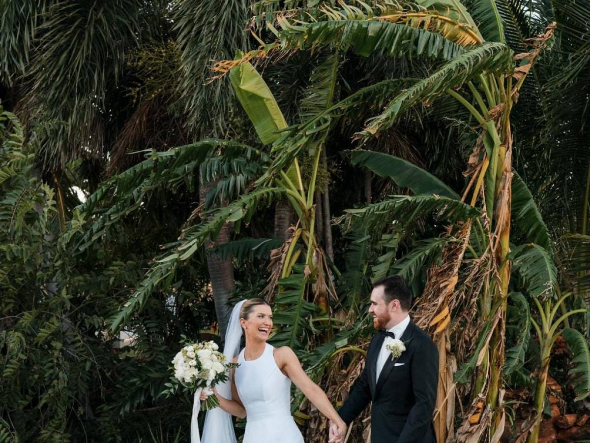 Bride and groom holding hands in front of lush tropical plants.