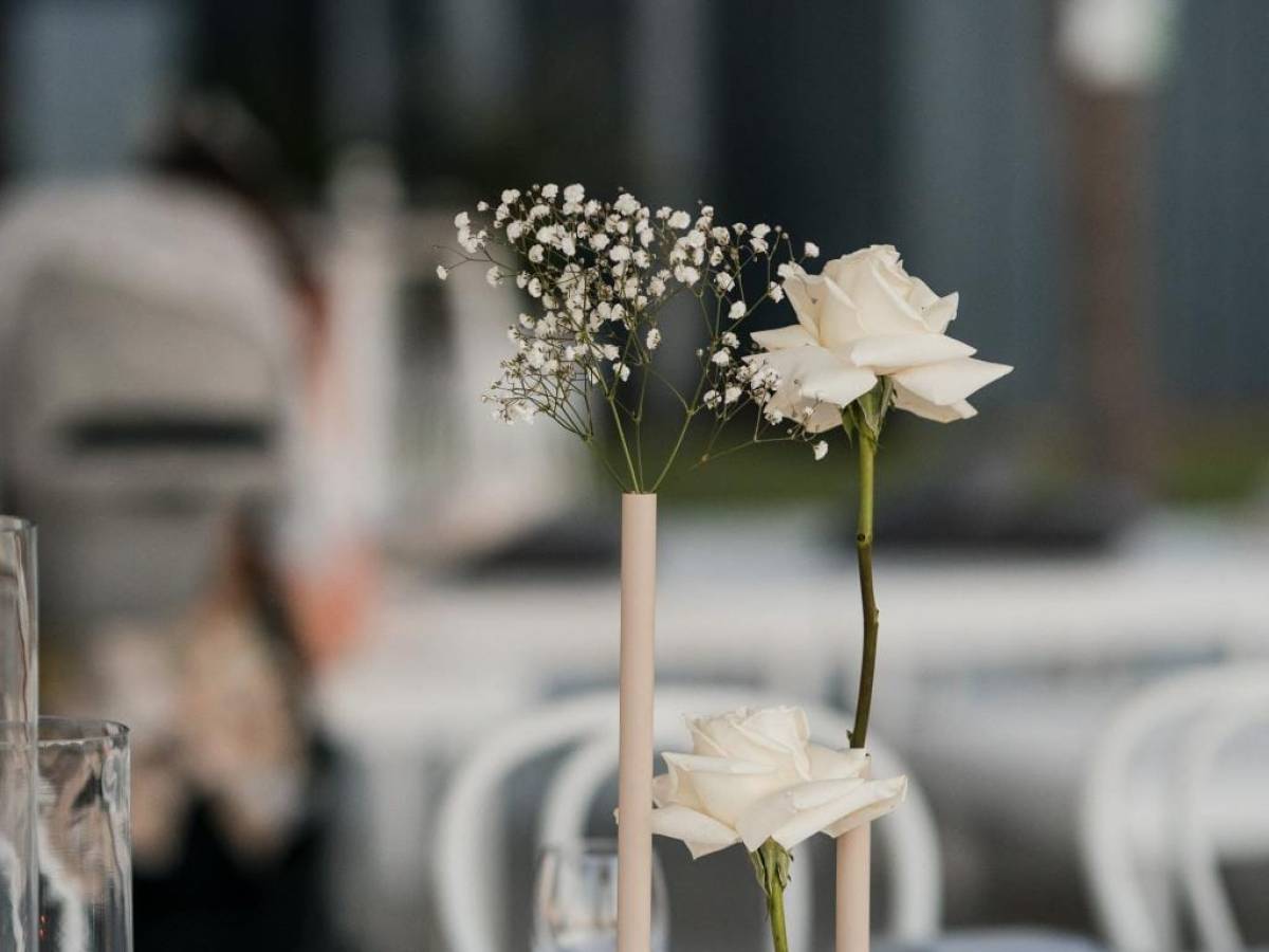 White roses and baby's breath in vases on a table with blurred lights in background.