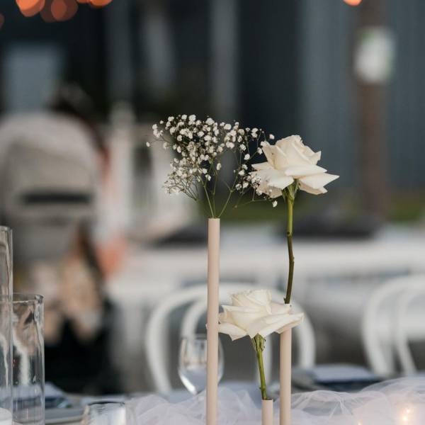 White roses and baby's breath in vases on a table with blurred lights in background.