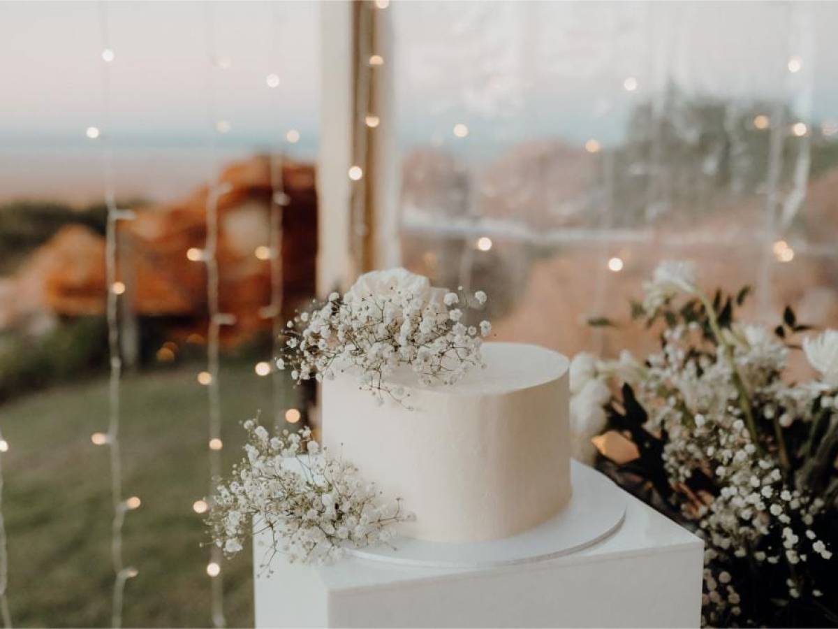 Wedding cake with white flowers and fairy lights in soft focus background.