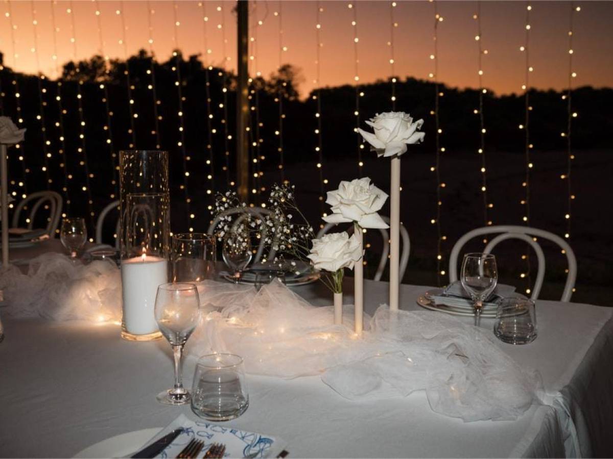 Elegant table setting with white roses, candles, and twinkle lights at sunset.