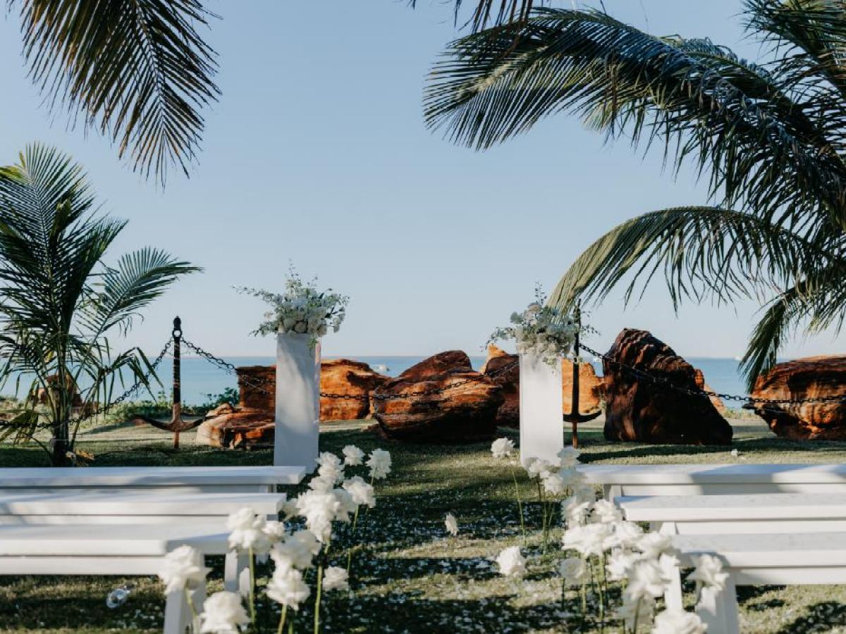 Outdoor wedding setup by the beach with palm trees and white flowers.