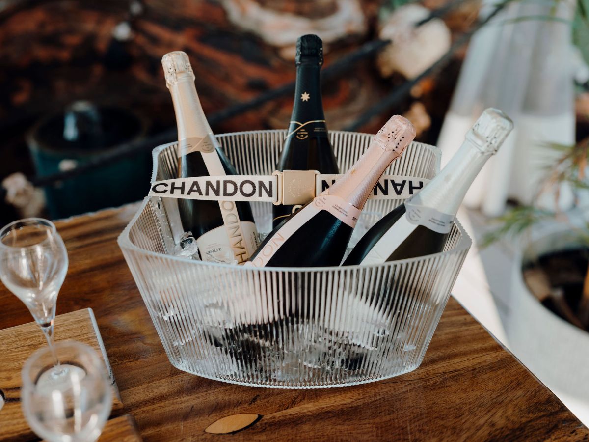 Four bottles of Chandon sparkling wine in a clear ice bucket on a wooden table.