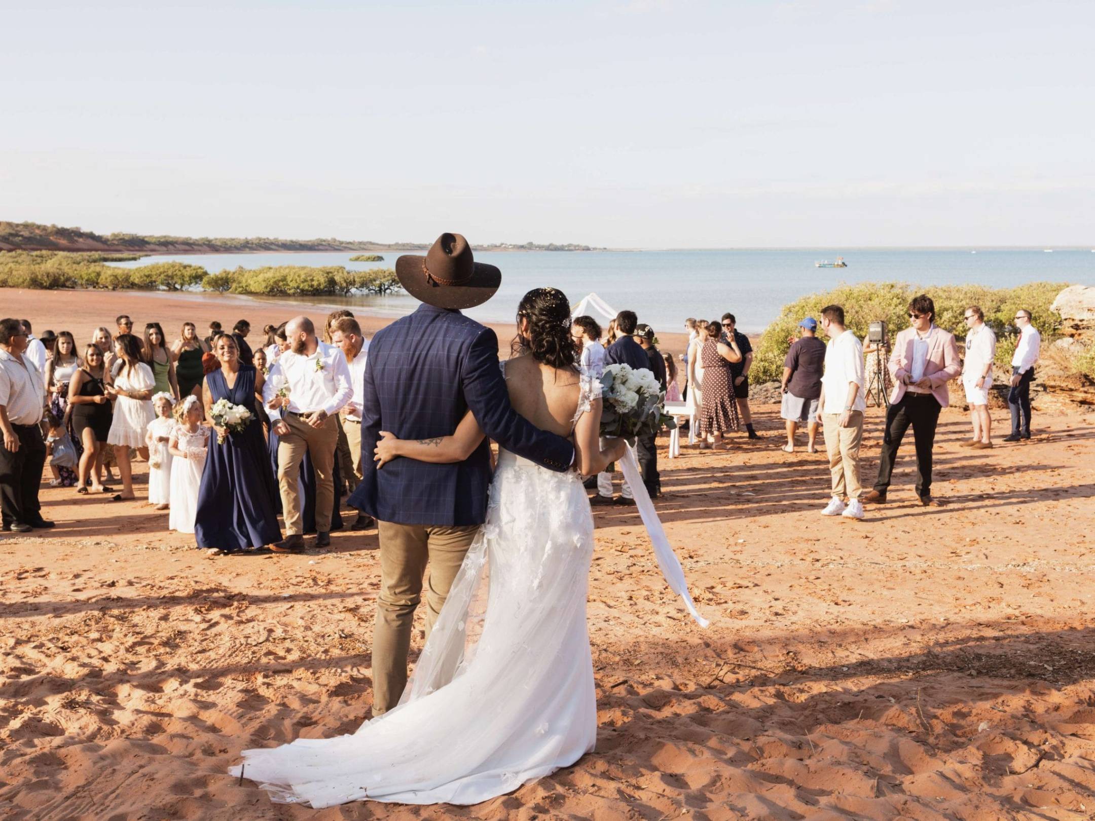 Wedding couple facing guests on a sandy beach with ocean in the background.