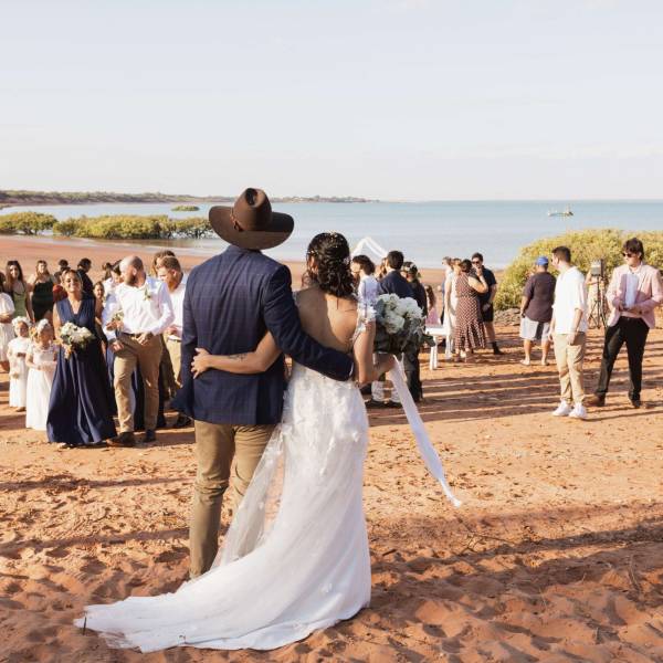 Wedding couple facing guests on a sandy beach with ocean in the background.