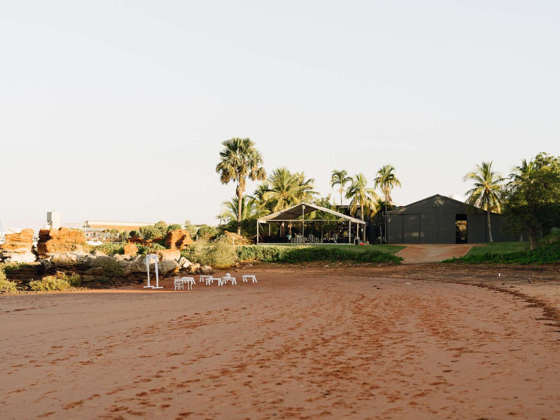 Sandy beach with palm trees and a building in the background.