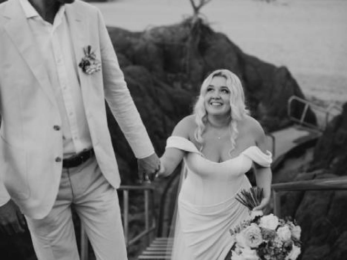 Bride and groom walk up rocky stairs, bride holding bouquet, both smiling at each other.