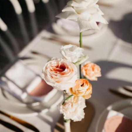Elegant table setting with pink and white roses centerpiece on a white tablecloth.