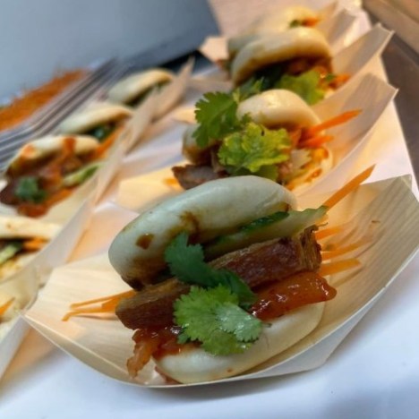 Row of bao buns with meat, cilantro, and carrots in small trays.