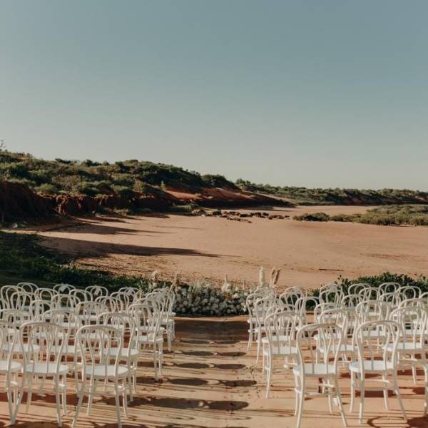 Outdoor wedding setup with white chairs facing an empty sandy landscape and clear sky.