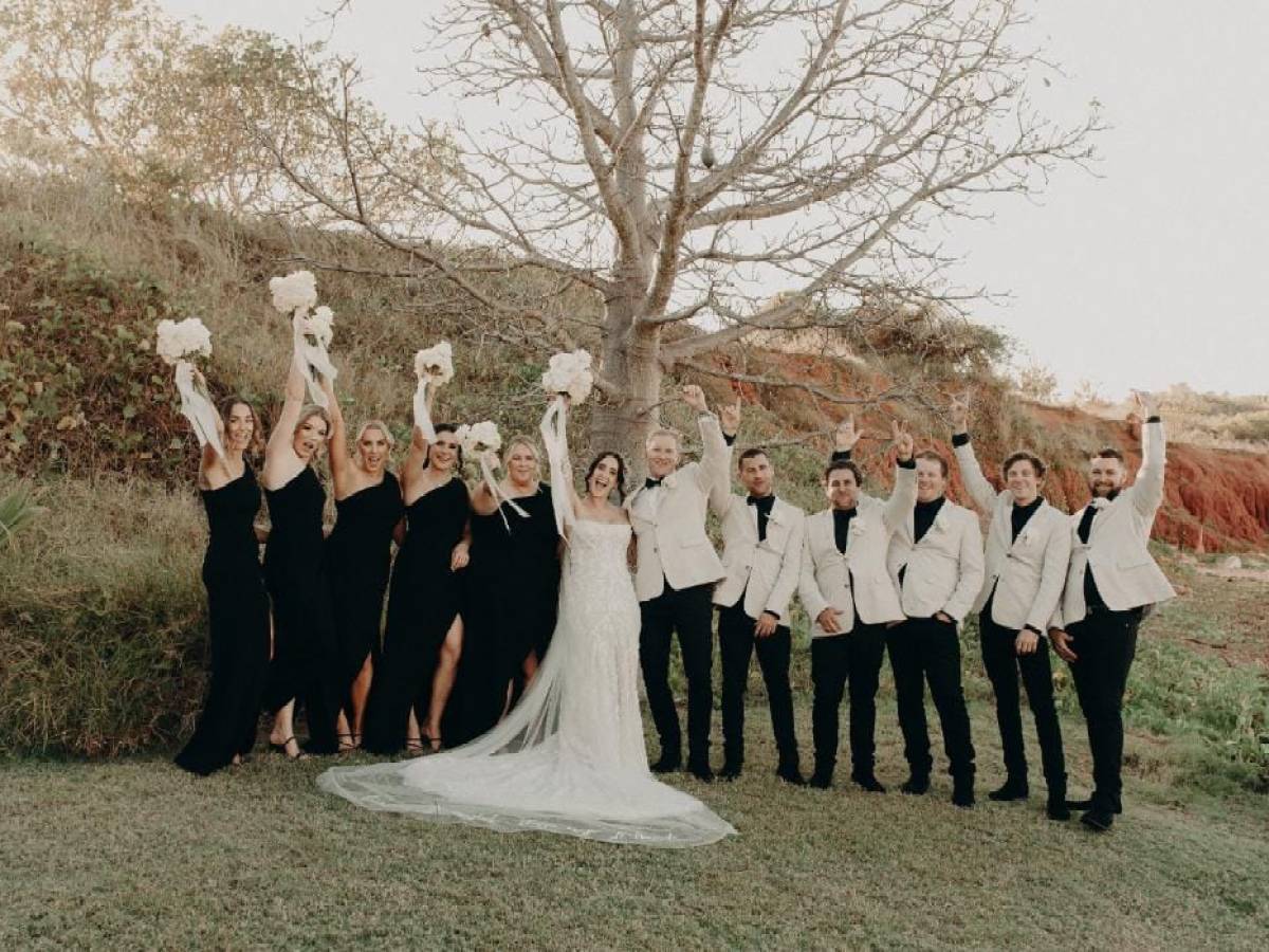 Wedding party in black and white attire poses cheerfully under a leafless tree.