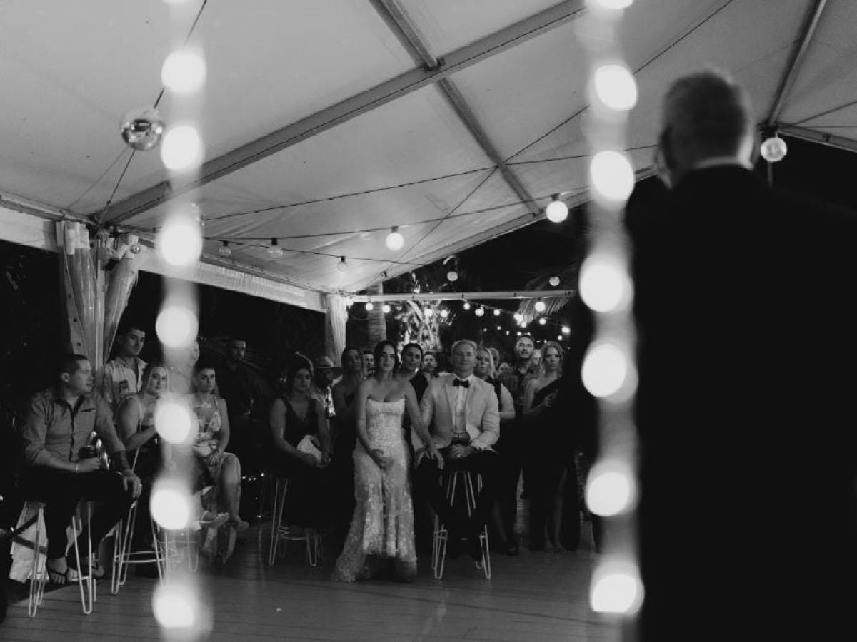 Black and white photo of a wedding reception under a tent with guests seated and standing.
