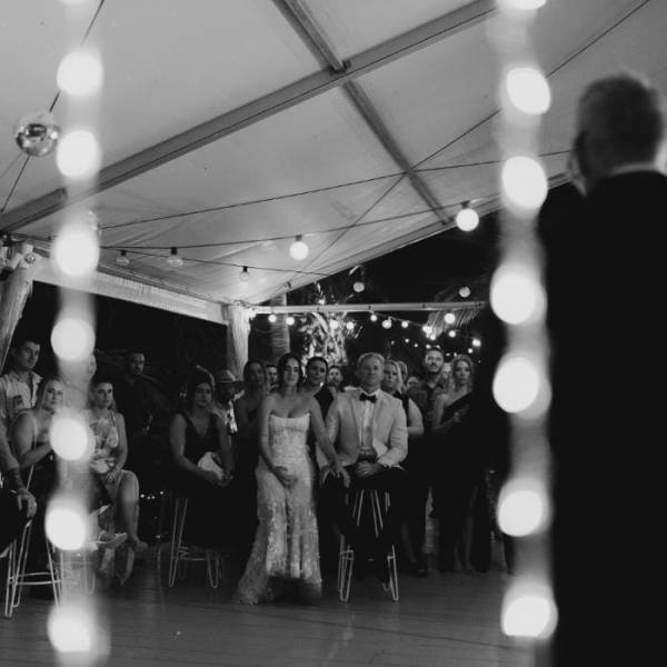 Black and white photo of a wedding reception under a tent with guests seated and standing.