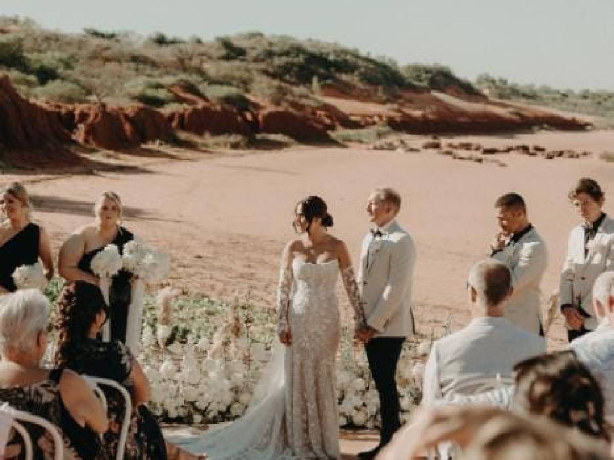 Outdoor wedding ceremony with a couple holding hands, surrounded by guests, against a desert backdrop.