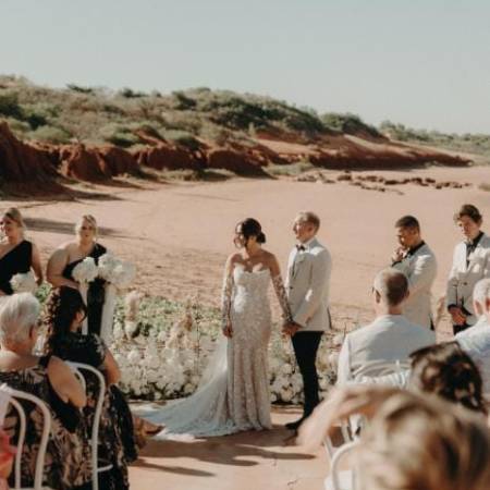 Outdoor wedding ceremony with a couple holding hands, surrounded by guests, against a desert backdrop.