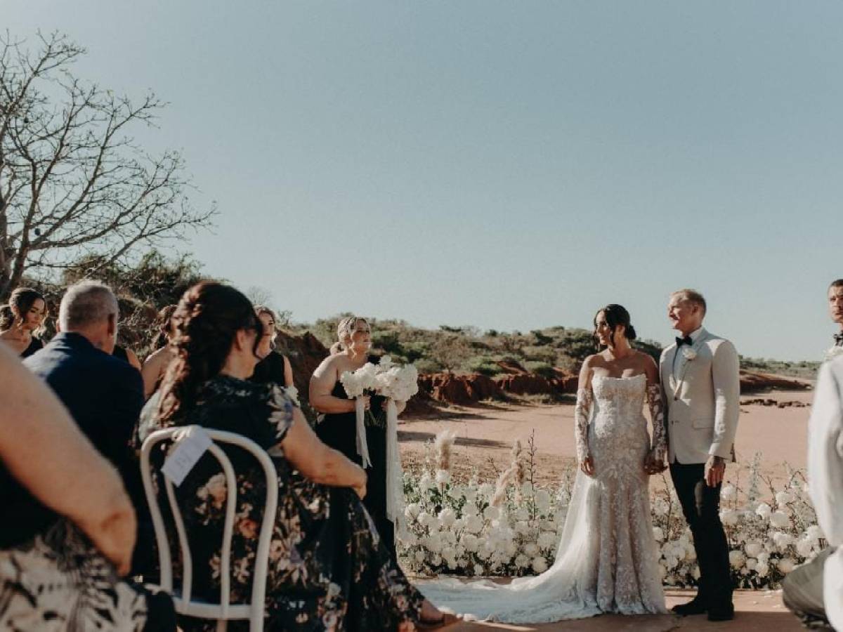 Outdoor wedding ceremony with a couple holding hands and guests seated.
