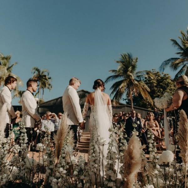 Outdoor wedding ceremony with bride, groom, and guests surrounded by palm trees.