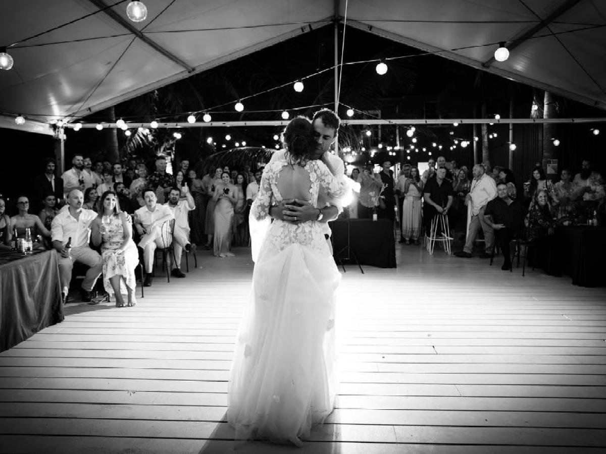 Bride and groom share first dance under string lights, surrounded by wedding guests.