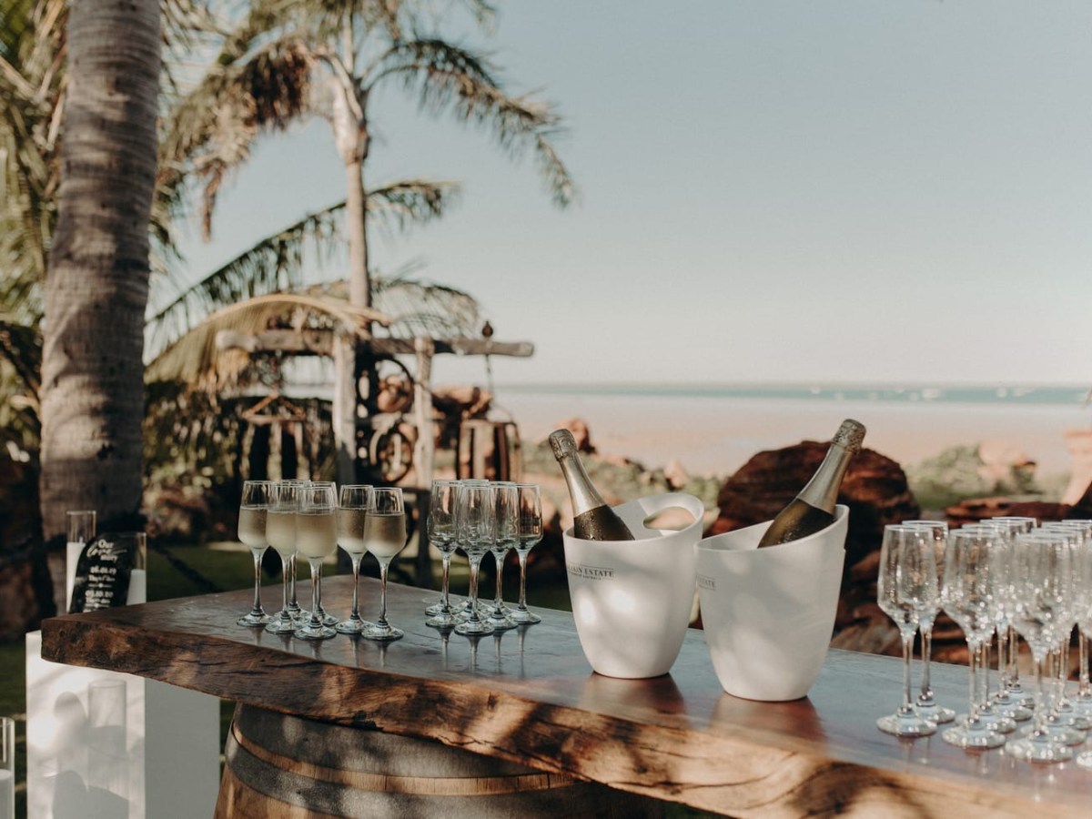 Outdoor bar with champagne glasses and palm trees near a beach.