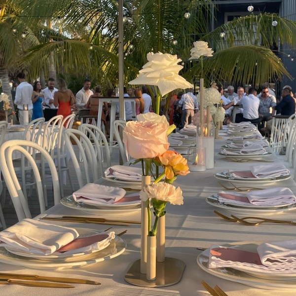 Elegant outdoor table setting with plates, napkins, flowers, and palm trees in the background.
