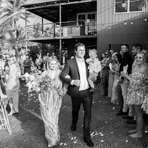 Black and white photo of a couple with a child in a celebratory outdoor gathering.