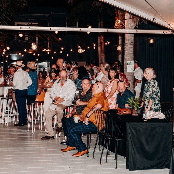 A lively outdoor gathering with people sitting and standing under string lights.