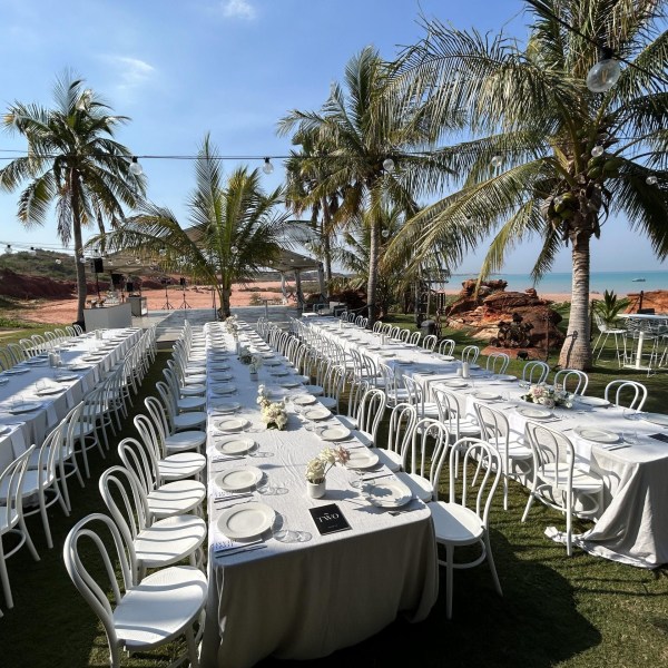 Outdoor tables set for dining under palm trees by the ocean.
