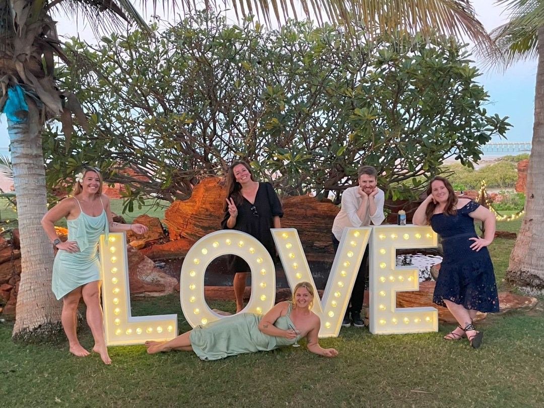 Five people posing with large illuminated 'LOVE' sign outdoors.