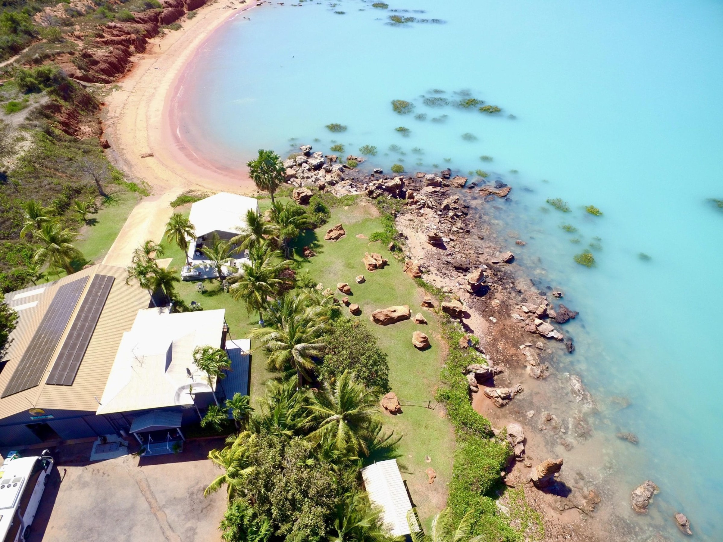 Aerial view of a coastal area with buildings, trees, rocks, and a blue ocean.