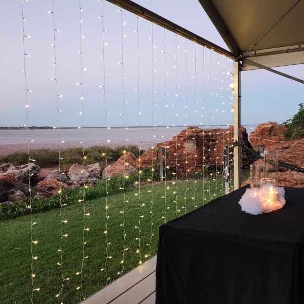 Outdoor pavilion with string lights, overlooking water and rocky landscape at dusk.