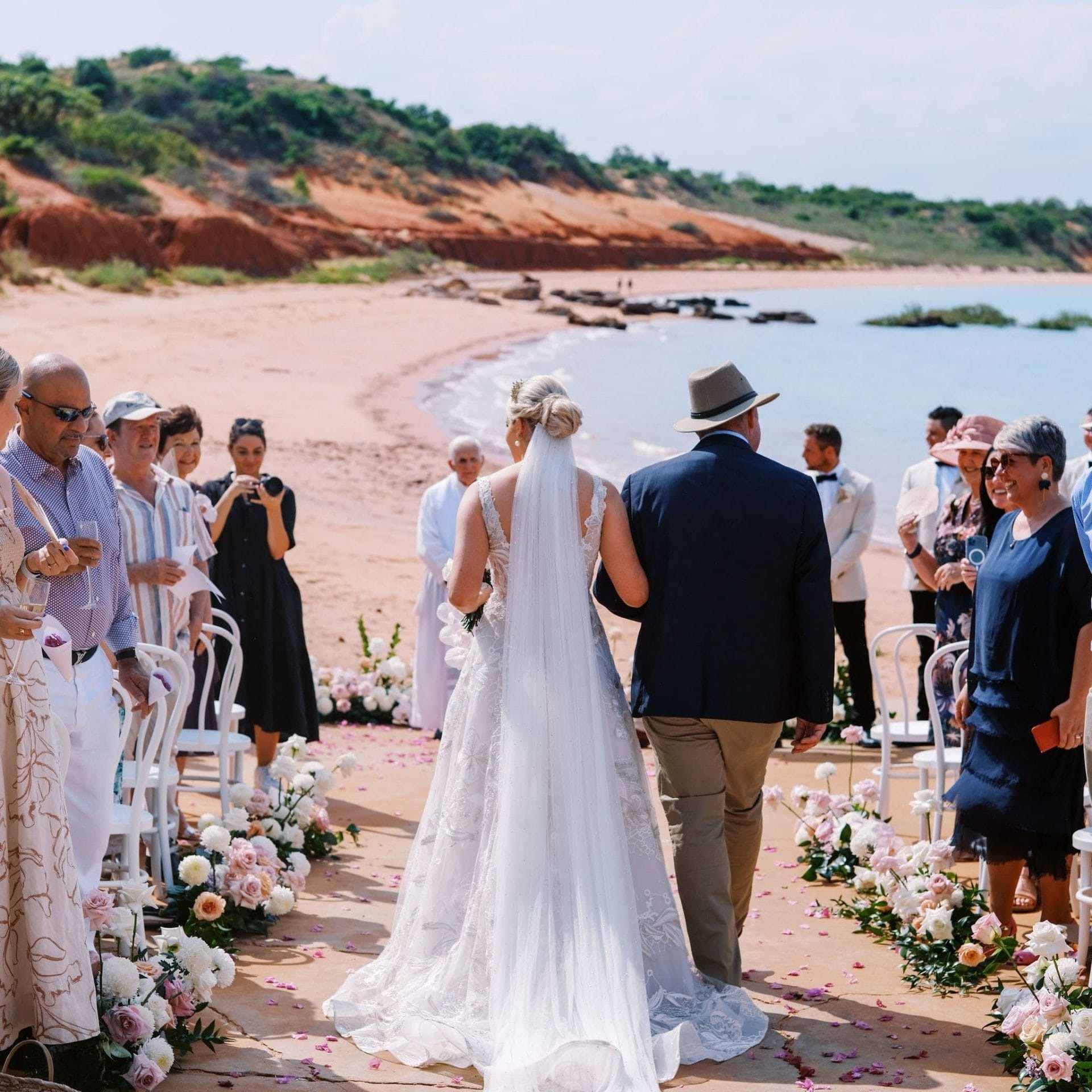 Bride and man walking down aisle on beach at outdoor wedding ceremony.