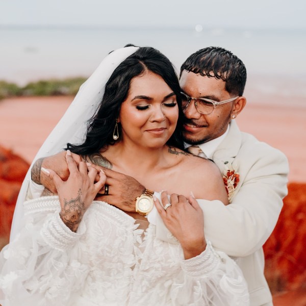 Bride and groom embrace in a desert setting with red earth and blue sky.