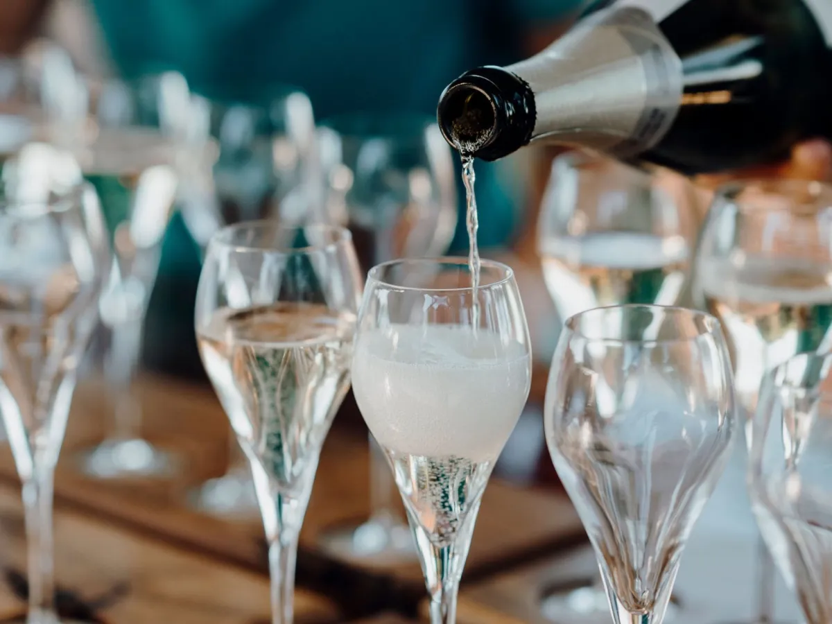 Champagne being poured into a row of glasses on a wooden tray.