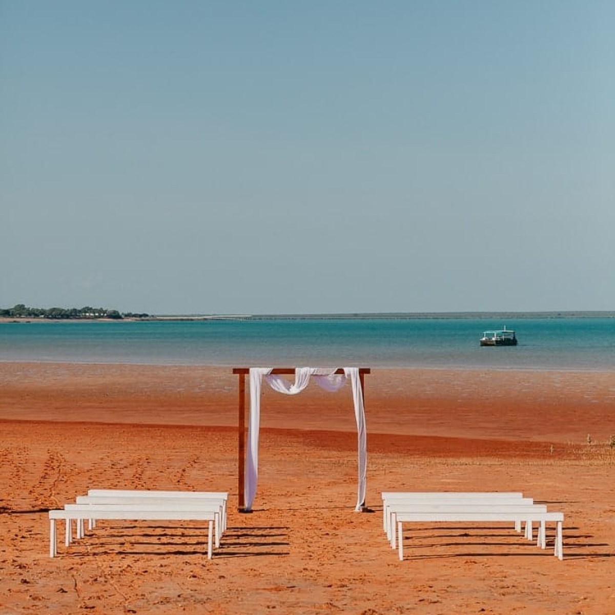 Beach wedding setup with wooden arch and benches on a sandy shoreline.