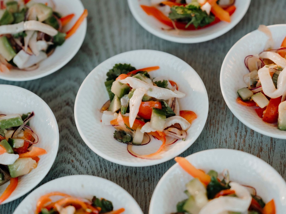 Small white bowls of mixed vegetable salad with cucumbers and carrots on a wooden table.