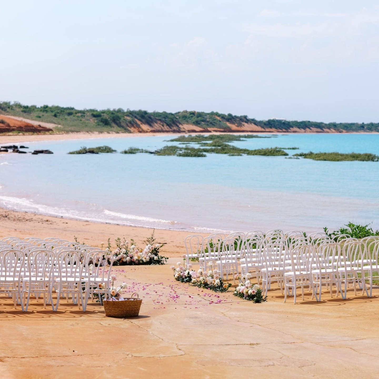 Beach wedding setup with white chairs and flowers overlooking the ocean.