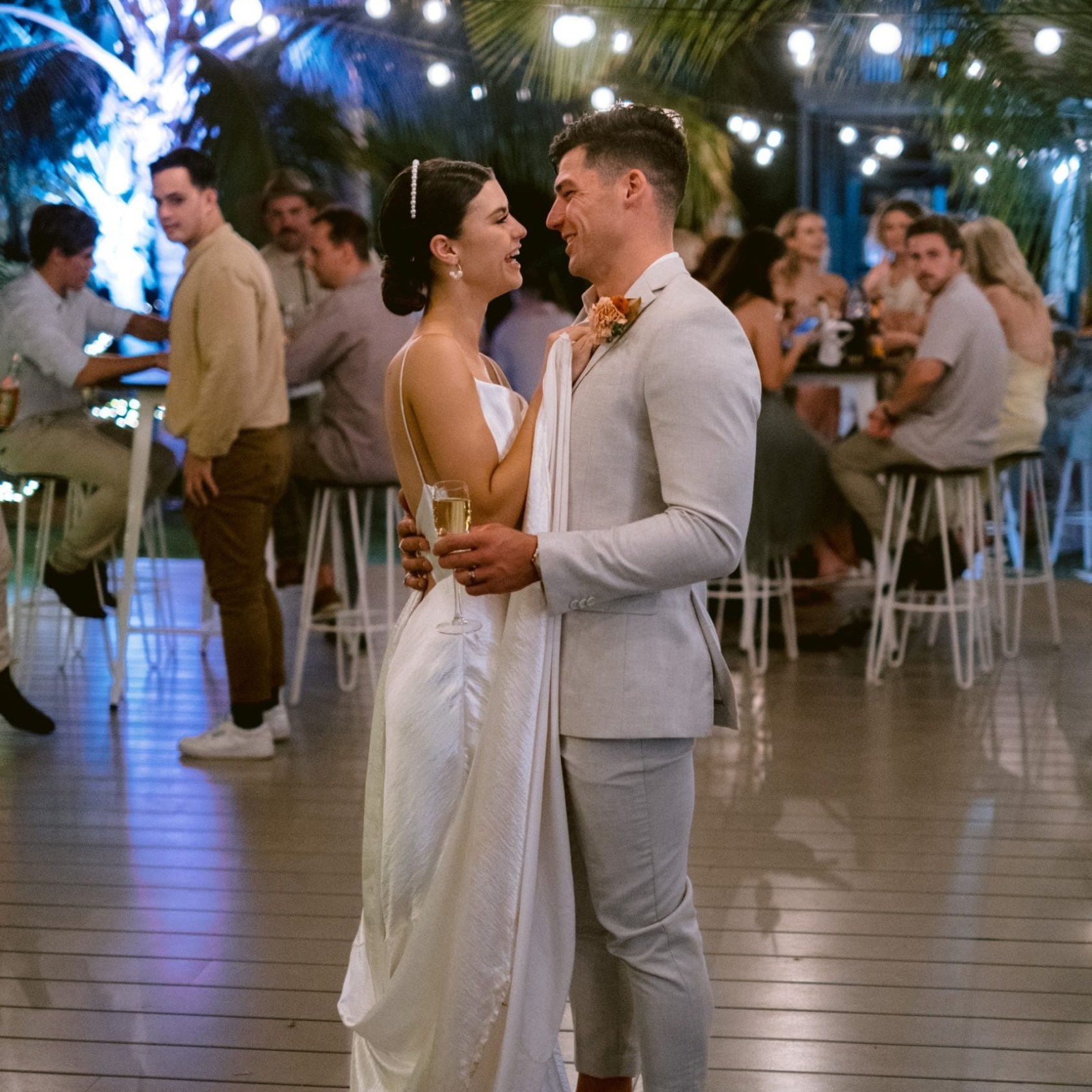 Newlyweds dancing under string lights at a tropical wedding reception.
