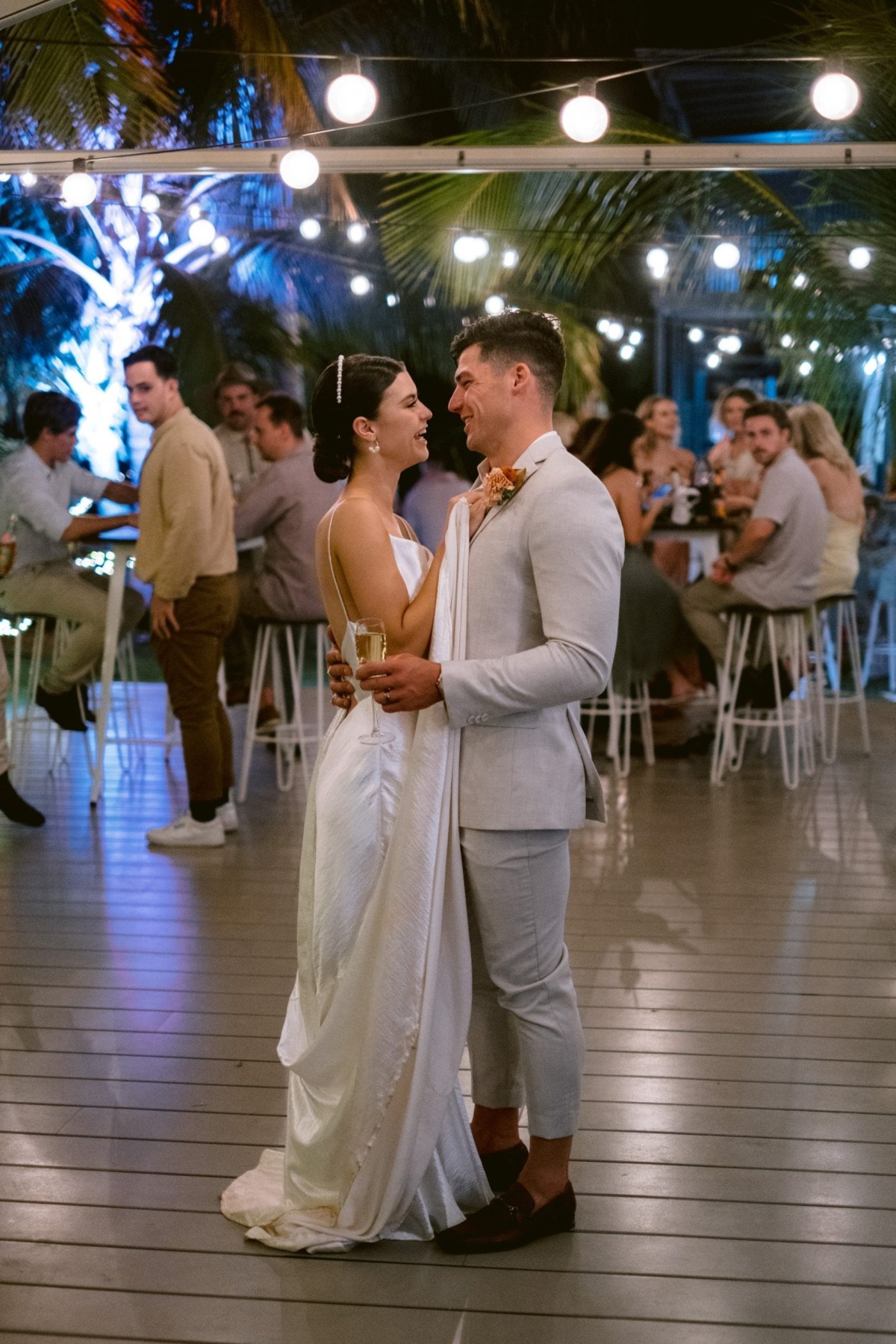 Newlyweds dancing under string lights at a tropical wedding reception.