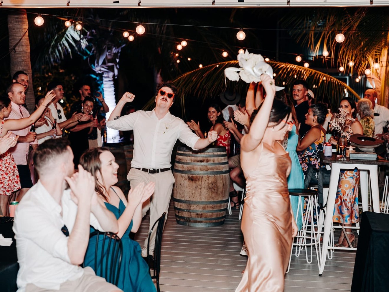 People dancing and celebrating at an outdoor party with string lights.