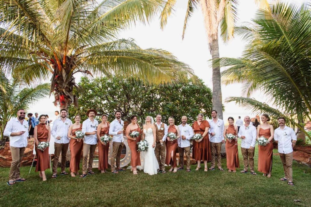 Wedding party in brown attire with bouquets under palm trees on a sunny day.
