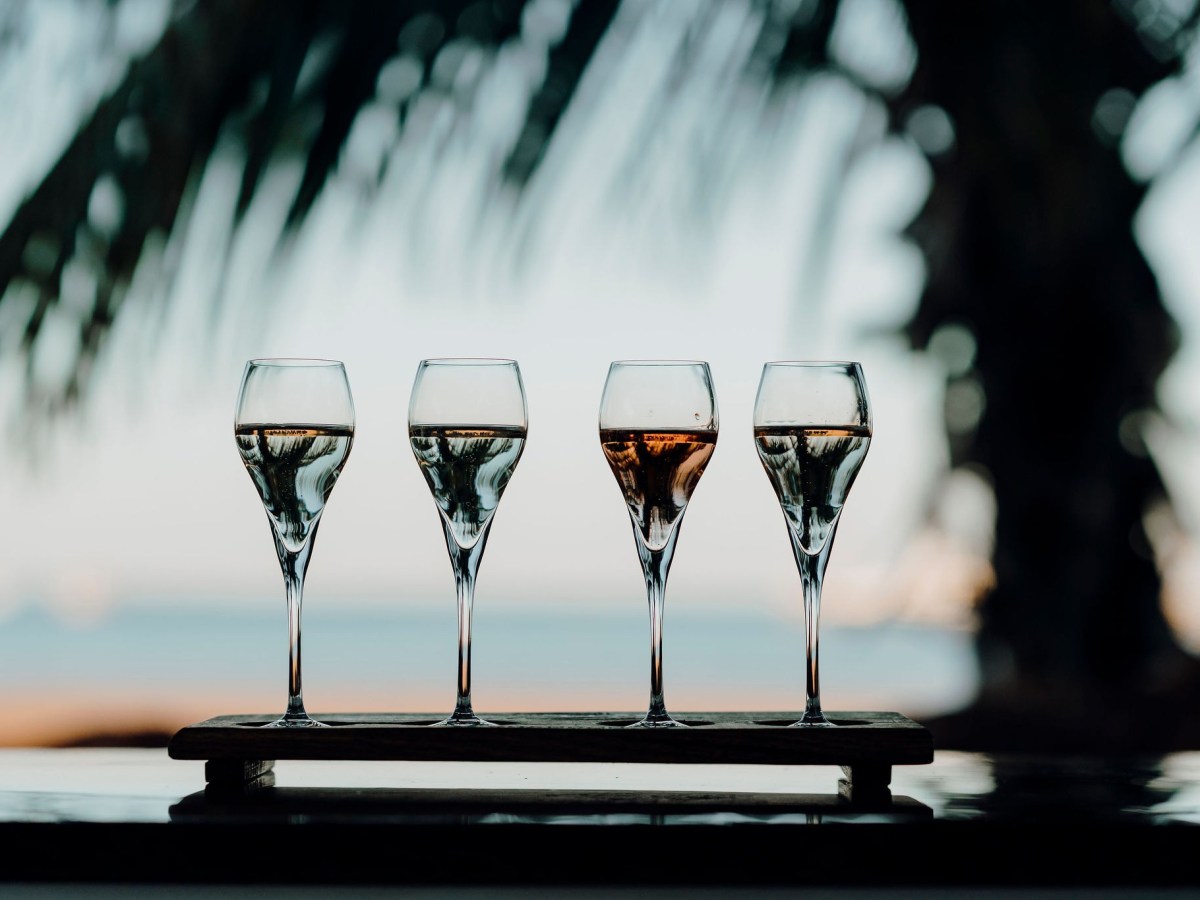 Four champagne glasses with liquid on a tray, palm trees blurred in background.