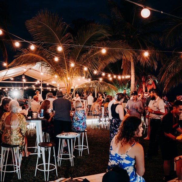Outdoor evening gathering with people under string lights and palm trees.