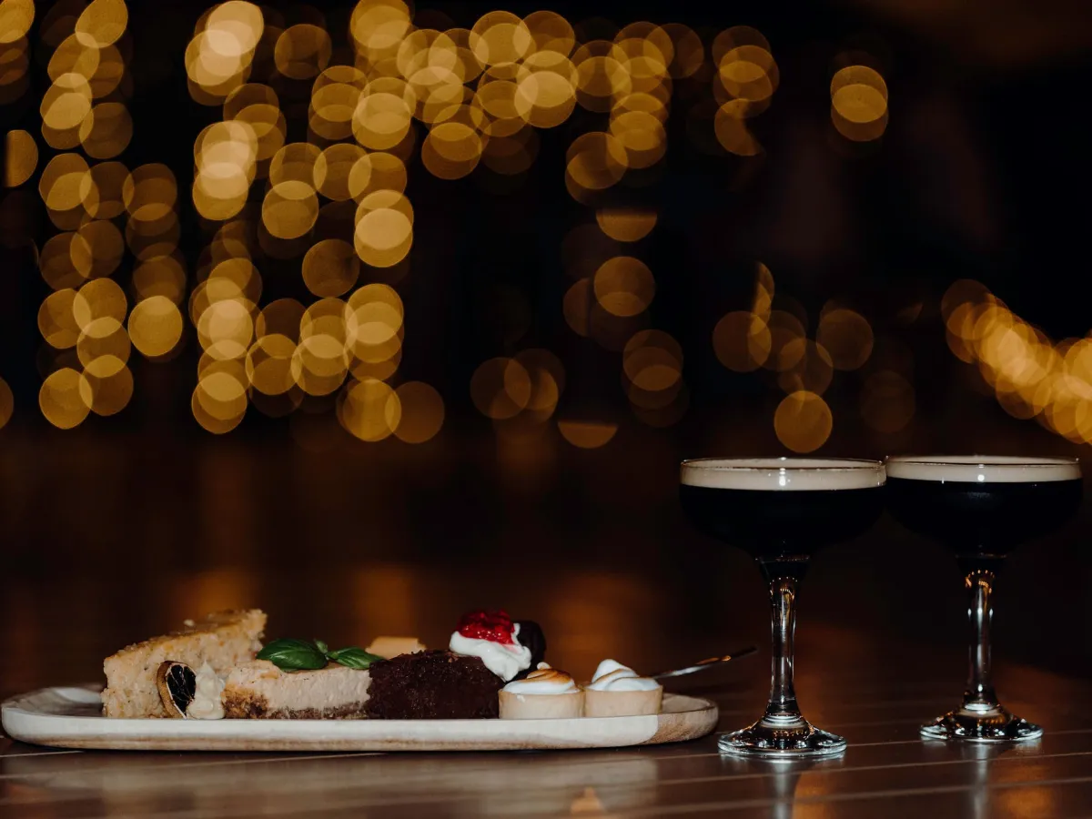 Desserts and espresso martinis on a table with bokeh lights in background.