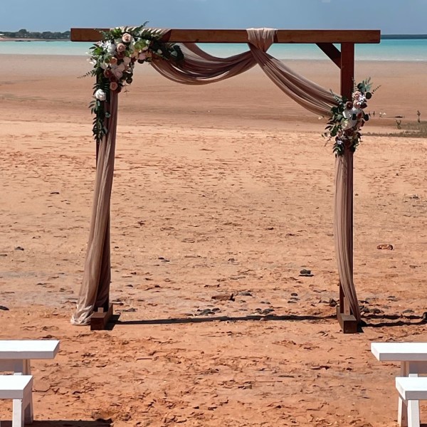 Beach wedding arch adorned with flowers and fabric, overlooking the ocean.